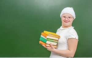 A girl with Down Syndrome standing near a school board with book